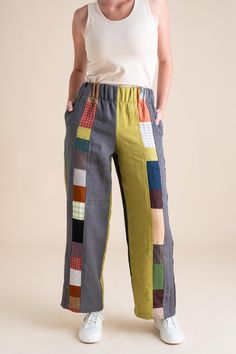 a woman standing in front of a white wall wearing pants with multicolored squares on them