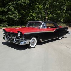 an old black and red convertible car parked in a parking lot with trees in the background