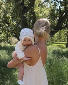 a woman holding a baby in her arms while wearing a white dress and headband