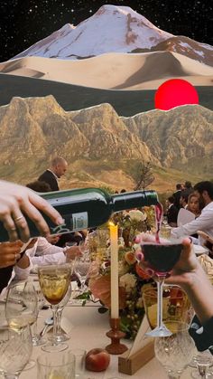 a group of people sitting around a table with wine glasses on it and mountains in the background