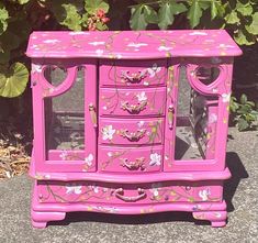 a pink dresser sitting on top of a sidewalk next to a bush with flowers painted on it