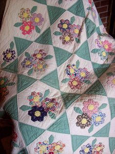 a quilt with flowers on it sitting on top of a table next to a brick wall