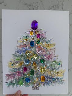 a hand holding up a card with a christmas tree made out of colored glass stones