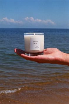 a hand holding a candle in front of the ocean