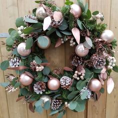 a wreath with pink and green ornaments hanging on a wooden wall next to a fence