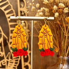 pair of earrings with red roses on them in front of a vase and wall decoration