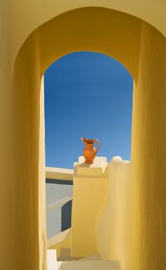 an orange vase sitting on top of a white wall next to stairs with blue sky in the background