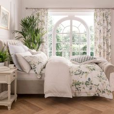 a bedroom with white walls and wooden flooring, large window overlooking the garden outside