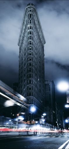 a very tall building sitting in the middle of a city at night with cars passing by