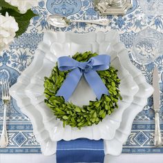 a white plate topped with a blue ribbon and a green wreath on top of it