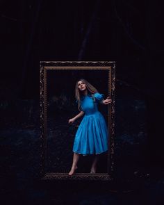 a woman standing in front of a mirror with her hands on her hips, wearing a blue dress