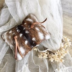 a cow skin mouse laying on top of a white lace covered table cloth next to dried flowers