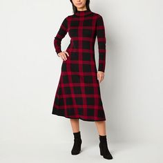 a woman wearing a black and red plaid dress with long sleeves, standing in front of a white wall