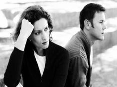 a man and woman sitting next to each other in the grass with their hands on their head