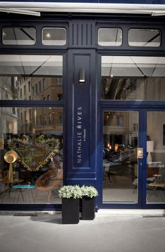 a store front with blue doors and plants in the window sill on the sidewalk