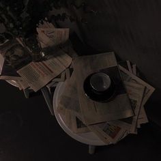 a table topped with lots of newspapers and a cup on top of it next to a plant