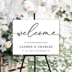 a welcome sign is standing in front of a flower filled area with white flowers and greenery