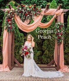 a woman in a wedding dress is standing under an arch with flowers and greenery