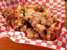 a basket filled with fried food sitting on top of a wooden table covered in red and white checkered paper