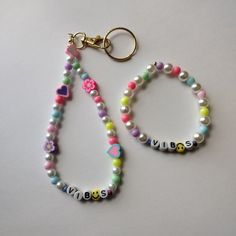 two bracelets with name beads and charms on white surface, one has a keychain