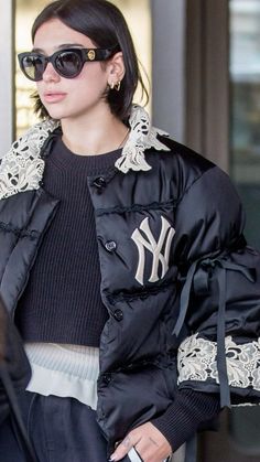 a woman in black jacket and sunglasses walking down the street with her hand on her hip