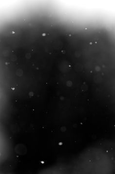 a black and white photo of snow falling on the ground with blurry trees in the background