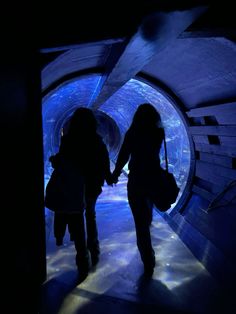 two people are walking through a tunnel with blue lights on the walls and in the dark