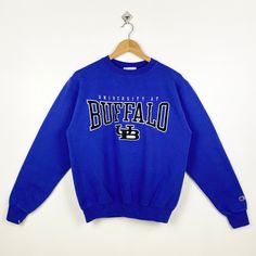 Vintage NCAA University at Buffalo 'Bulls' Crewneck Sweatshirt Embroidery Logo Blue Color Men's S - Made in Honduras - Materials : Cotton, Polyester - Tag Reads : S Kindly see the actual measurements (All measurements were taken lying flat) - Actual size manual measurements * Width (Armpit to armpit) : 21 inches * Length (Shoulder to end of garment) : 24.5 inches * Sleeve length : 25 inches - Condition : * Good condition 8/10 (80%)  * Minor stain refer picture  * Free from tear and major defect Collegiate Blue Top With Embroidered Logo, University At Buffalo, Buffalo Bulls, Sweatshirt Embroidery, Embroidery Sweatshirt, Fedex Express, Fancy Dresses, Dhl Express, Embroidery Logo