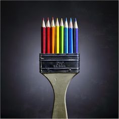 a group of colored pencils sitting on top of a paintbrush in front of a black background