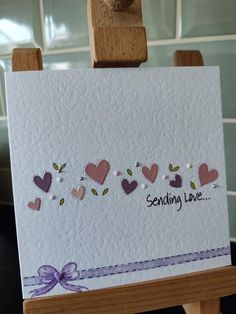 an easel holding a greeting card with hearts on it and the words sending love