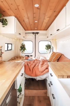 an interior view of a camper with wood ceiling and white cabinets, bed in the foreground