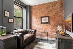 a living room filled with furniture and a brick wall behind the couch is a fish tank