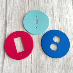 two blue and one red buttons sitting on top of a wooden table next to each other