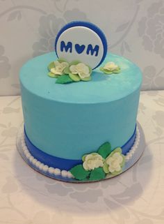 a blue cake with white flowers and a mom sign on the top is sitting on a table