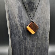 a necklace with a wooden pendant hanging from it's side on a piece of wood