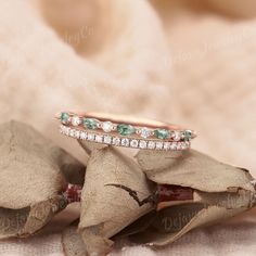 two wedding bands with green and white stones on top of each other in front of some leaves