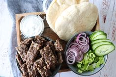 a wooden tray topped with meat and veggies next to a pita bread