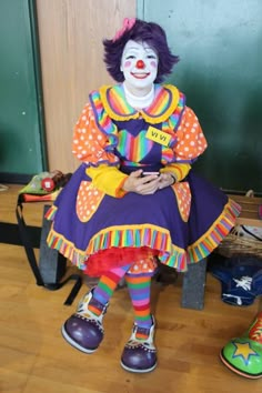 a clown is sitting on a chair with his legs crossed and head turned to the side