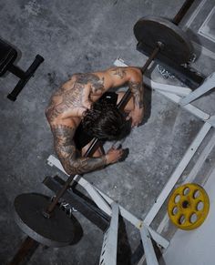 a man with tattoos on his back sitting in front of a barbell squatting machine