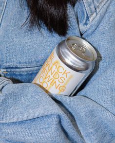 a person wearing a jean jacket and holding a can of beer in their lap with both hands