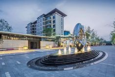 a fountain in the middle of a plaza with lights on it's sides and buildings in the background