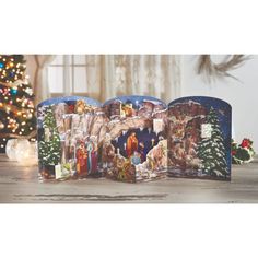 an open christmas card with the nativity scene on it in front of a christmas tree