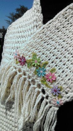 a white crocheted shawl with colorful flowers on the side and tassels