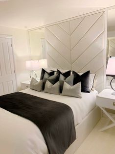 a bed with black and white pillows in a bedroom next to a mirror on the wall