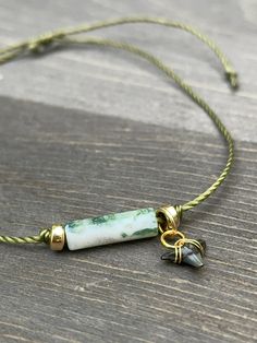 a green and white beaded necklace on a wooden table with a gold charm hanging from it's end