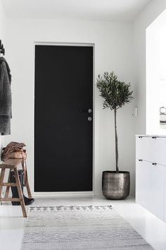 a black door in a white room with a stool and potted plant on the floor