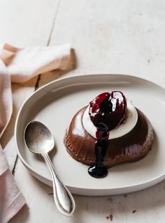 a white plate topped with a chocolate dessert covered in whipped cream and syrup next to a spoon