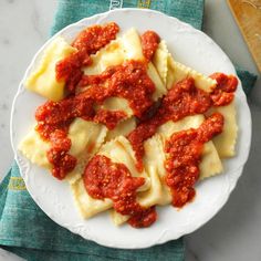 a white plate topped with ravioli covered in marinara sauce on top of a green napkin