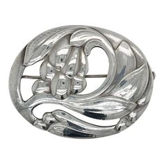 A fine antique Georg Jensen brooch or pin.  In sterling silver.  Model no. 65 with a floral motif.  Designed by Georg Jensen.  Together with its original box from Walter Muhke-Hofjuwelier Coblenz (Crown Jeweler).  Simply a wonderful brooch from one of Denmark's premier silversmiths!  Date: Early 20th Century  Overall Condition: It is in overall good, as-pictured, used estate condition.  Condition Details: There are two small spots of persistent tarnish to the reverse of the brooch. Otherwise, th Vintage White Gold Oval Brooches, Silver Hallmarked Oval Brooch, Classic Silver Brooches With Intricate Design, Silver Hallmarked Oval Brooches, Silver Oval Hallmarked Brooch, Silver Oval Brooches Hallmarked, Silver Engraved Brooches For Formal Occasions, Victorian Silver Oval Brooch, Classic Silver Engraved Brooches