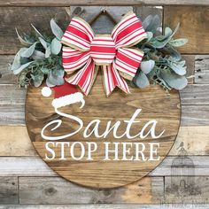 a wooden sign that says santa stop here with a red and white bow on it